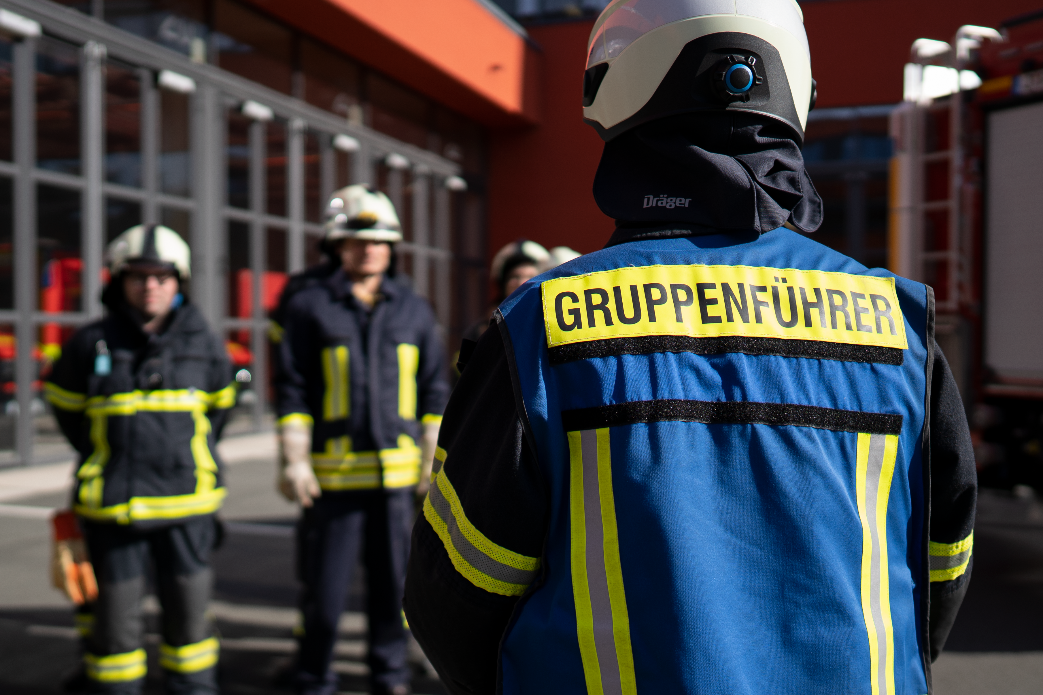Ein Gruppenführer der Feuerwehr von hinten steht seinen Kameraden gegenüber